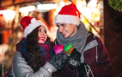Fotografia Happy Couple In Warm Clothes With Hot Drinks Enjoying Christmas Market At Evenin